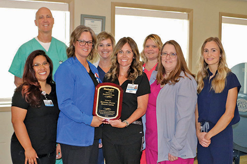 The wound clinic staff posing around their excellence award and smiling.