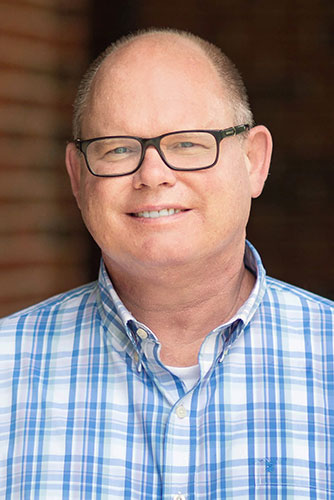 Dr. Paul Bassett - A close up photo of a man wearing glasses and a blue plaid button up dres shirt